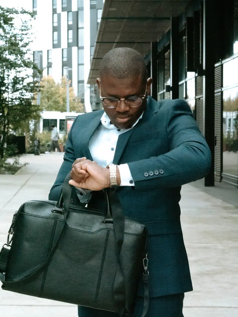 Homme d'affaires avec sacoche regardant sa montre devant un immeuble
