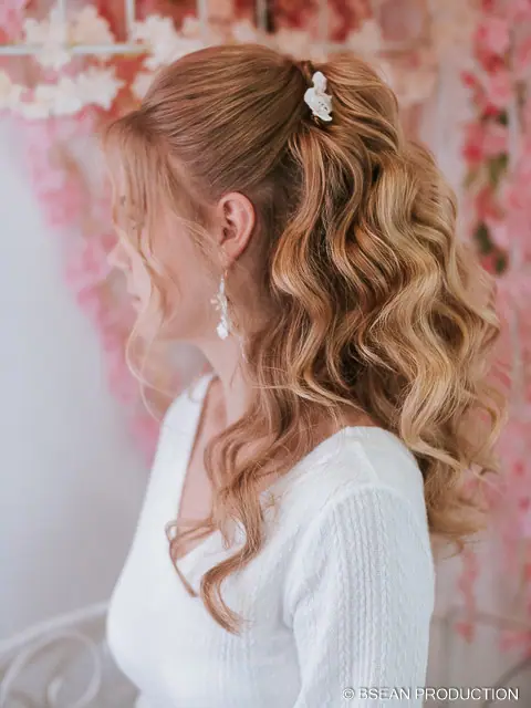 Invitée blonde de profil, coiffure ondulée, devant des fleurs roses