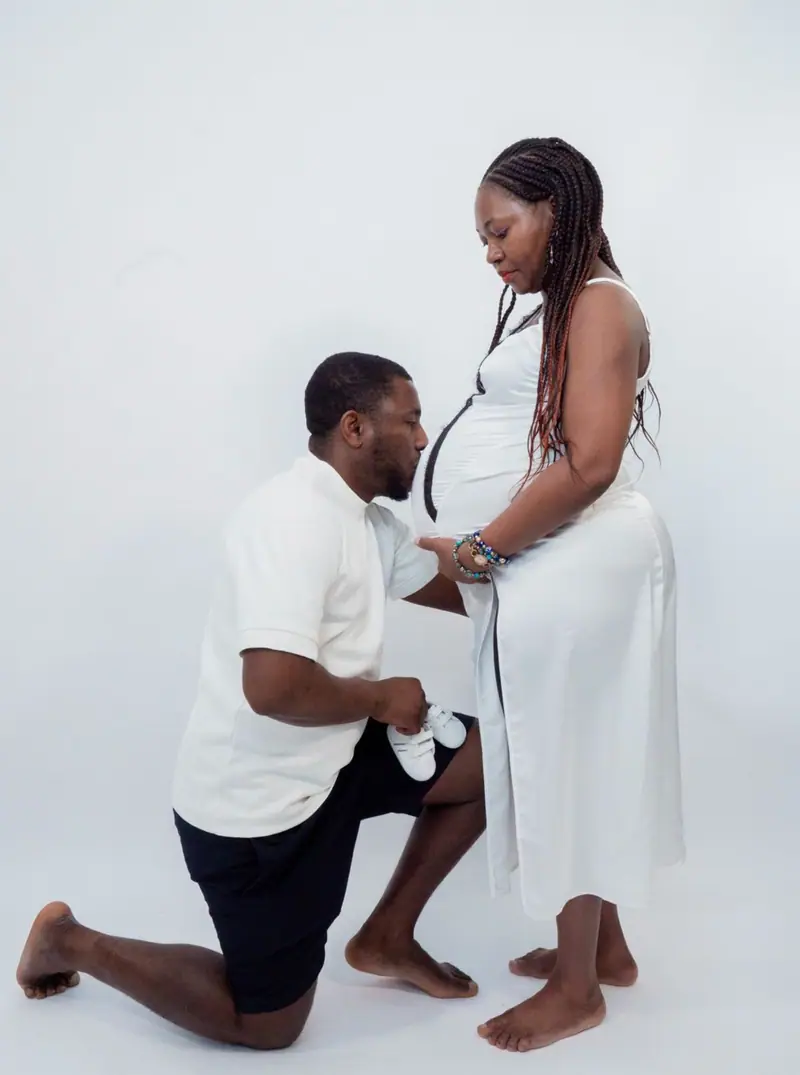 Futur papa à genoux embrassant le ventre de sa compagne en studio