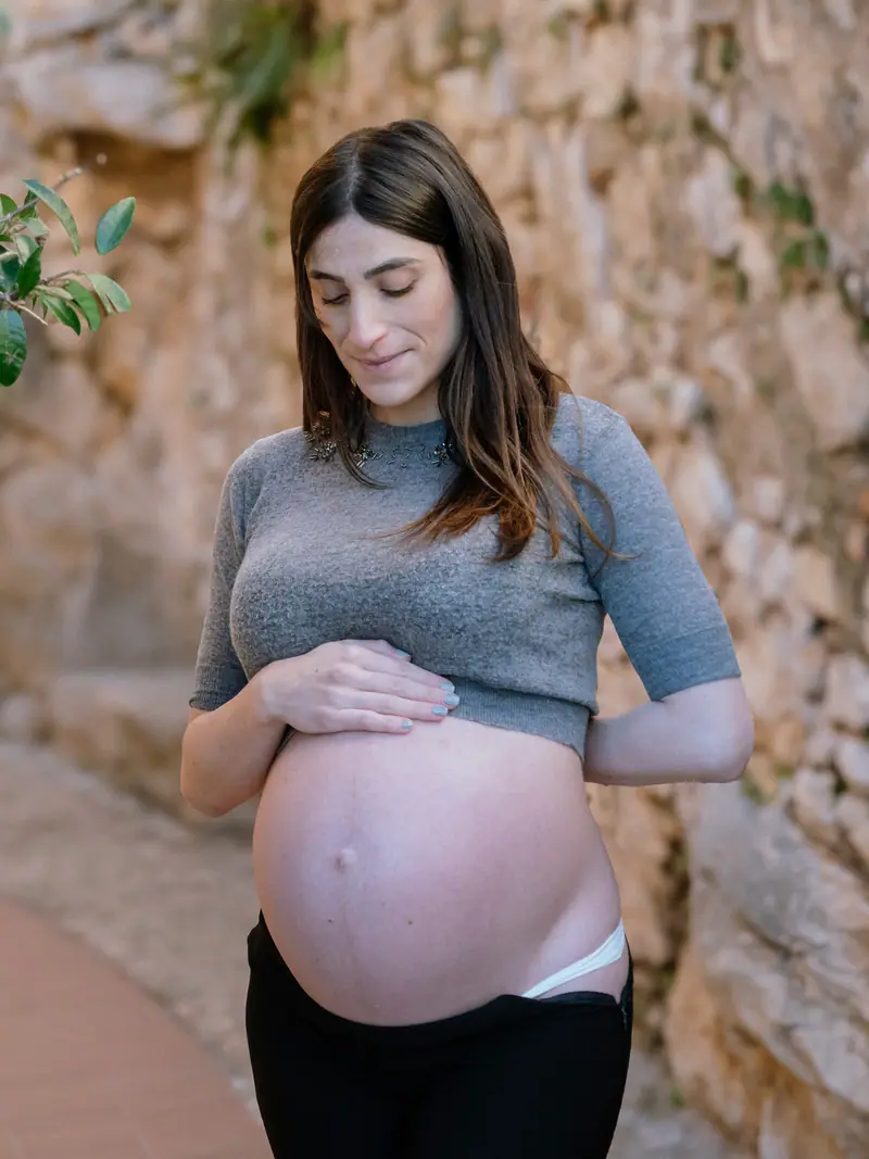 Future maman tenant son ventre devant un mur en pierre
