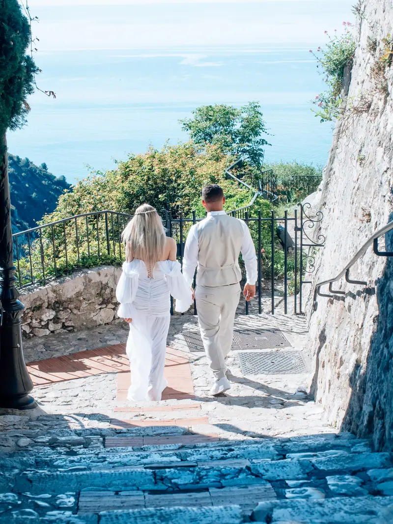 Couple de mariés en blanc marchant main dans la main dans une ruelle pavée en pierre
