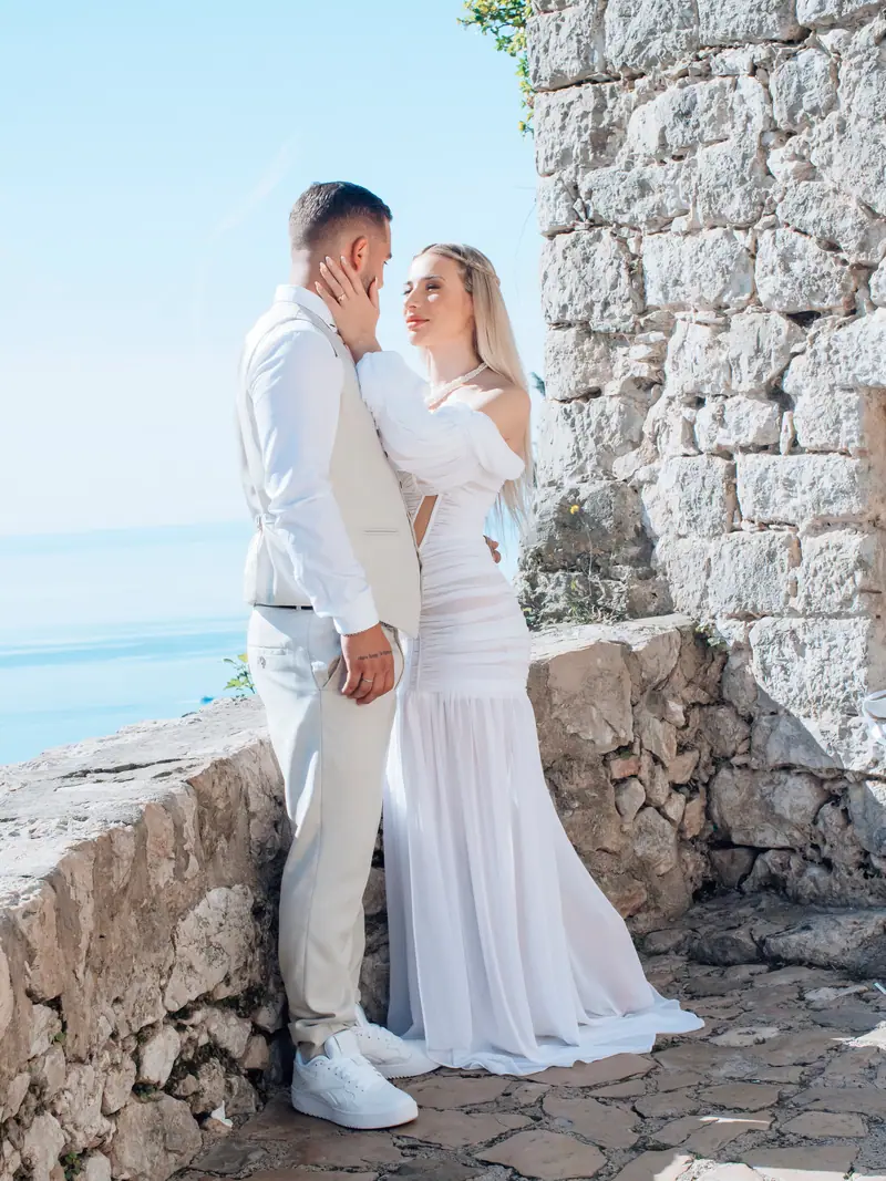 Couple de mariés enlacés devant un mur en pierre, Méditerranée à l'horizon