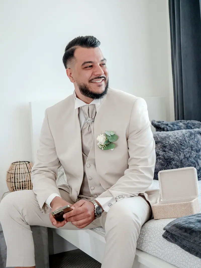 Marié en costume beige assis sur un canapé, sourire détendu pendant les préparatifs