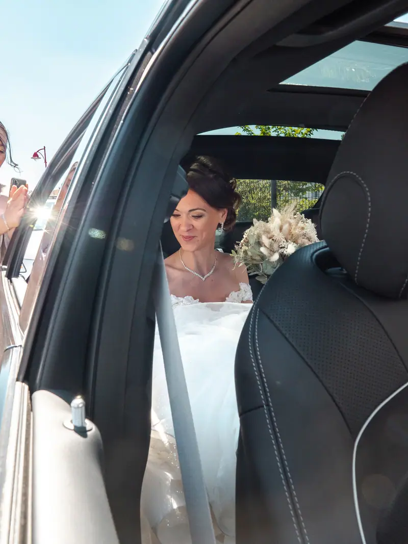 Mariée assise dans une voiture de luxe, bouquet sur les genoux
