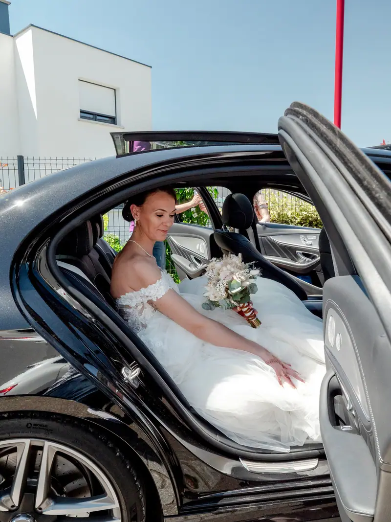 Mariée descendant d'une voiture noire portière ouverte, bouquet à la main