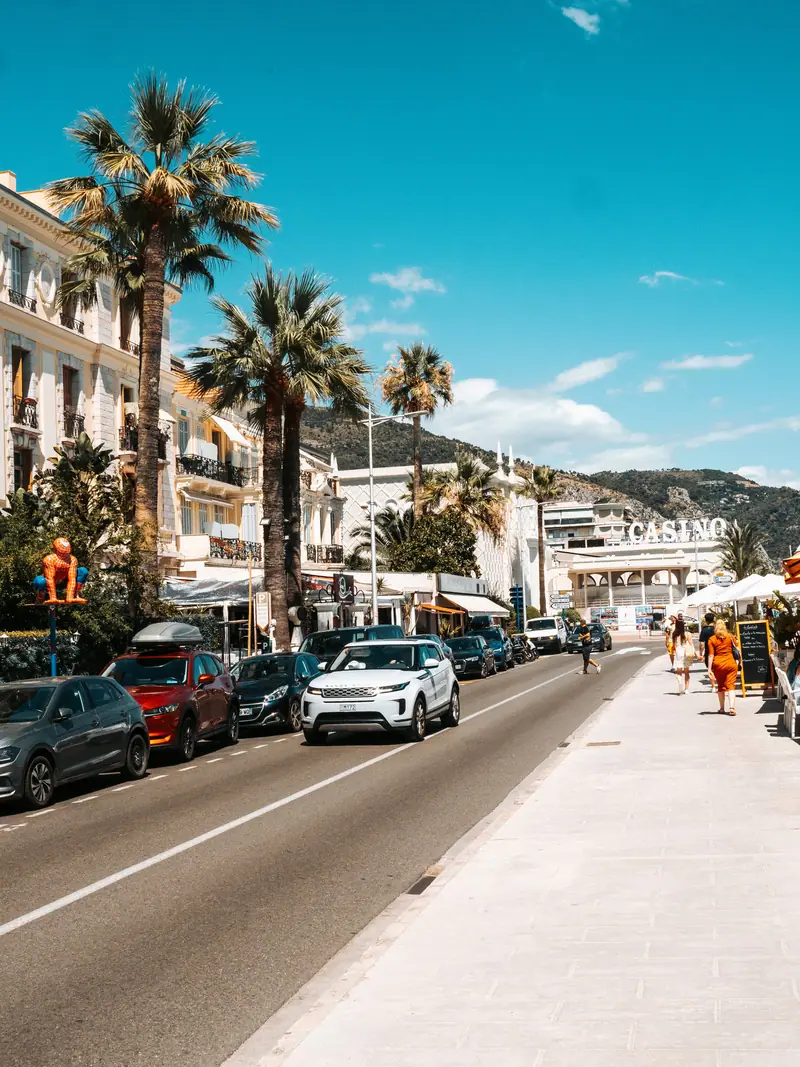 Avenue animée bordée de palmiers face aux collines de Menton